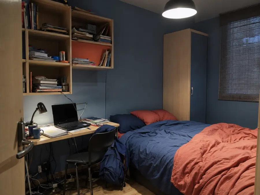 Chambre de lycéen encombrée avec bureau trop petit, câbles et éclairage agressif